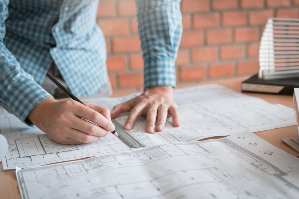 Engineering man standing examining working on blueprint.