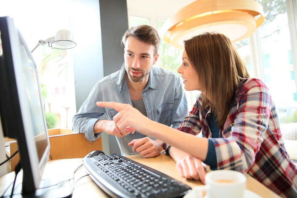 Couple in coffee shop websurfing on desktop computer
