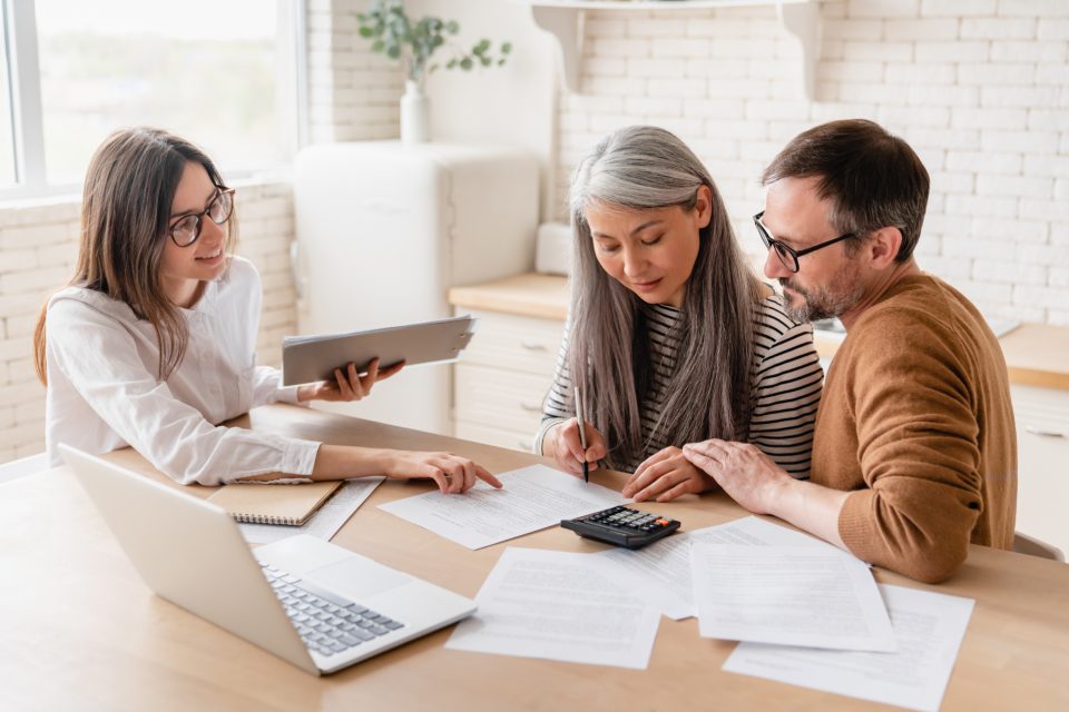 Insurance agent consulting mature family couple, discussing health insurance, signing contract deal of loan pension mortgage at home, calculating funds, investments, savings