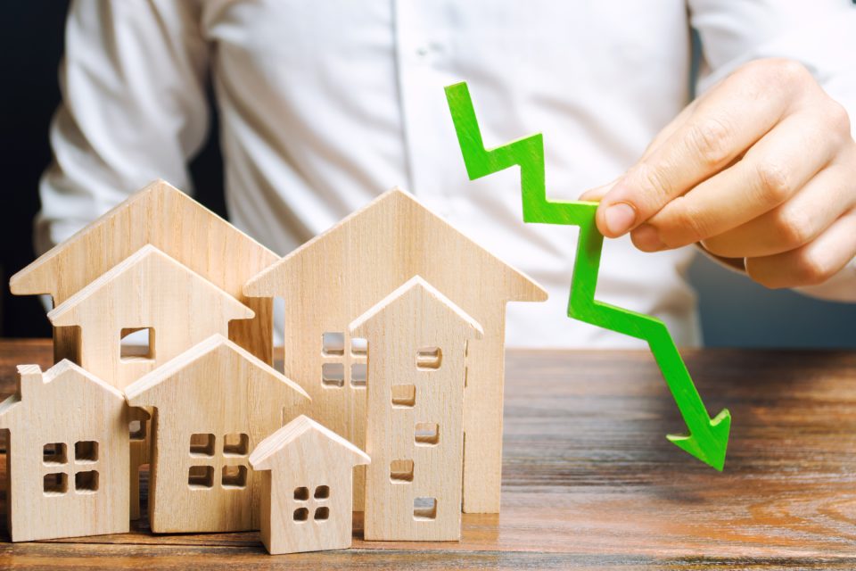 Analyst holds down arrow near the wooden houses. Concept of falling real estate market. Low prices and cost of housing. Reduced mortgage rates and housing demand. Bankruptcy. Crisis and low liquidity