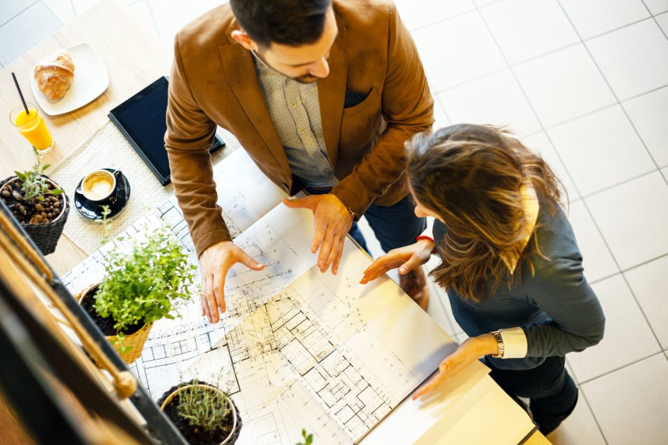 Two young architects discussing building plans during a meeting in a modern cafe. High angle view