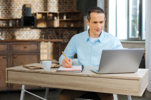 Making notes. Competent manager looking at his laptop and using pen while sitting at his workplace