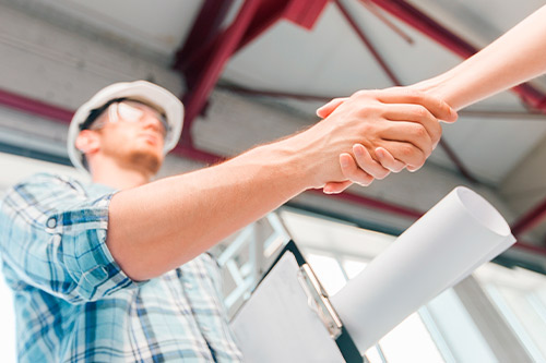 A man and woman shake hands over a blueprint, representing partnership and trust in McAllen's commercial construction industry.