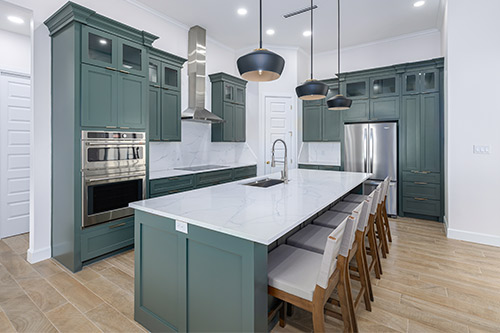 A modern kitchen featuring green cabinets and a sleek white countertop, showcasing current design trends.